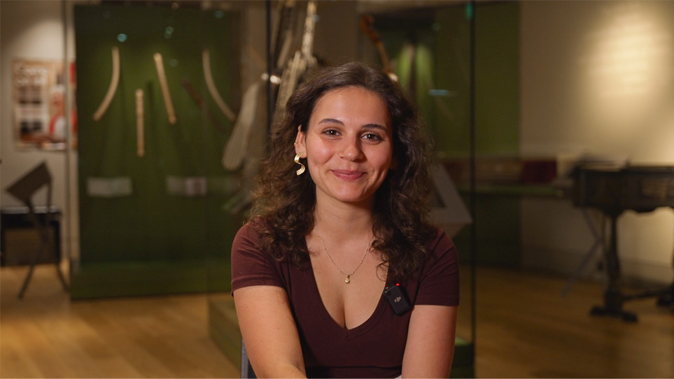 My application experience at the Royal College of Music A female student, with dark curly hair, smiling at the camera, sitting in a room with ornate and historical instruments.